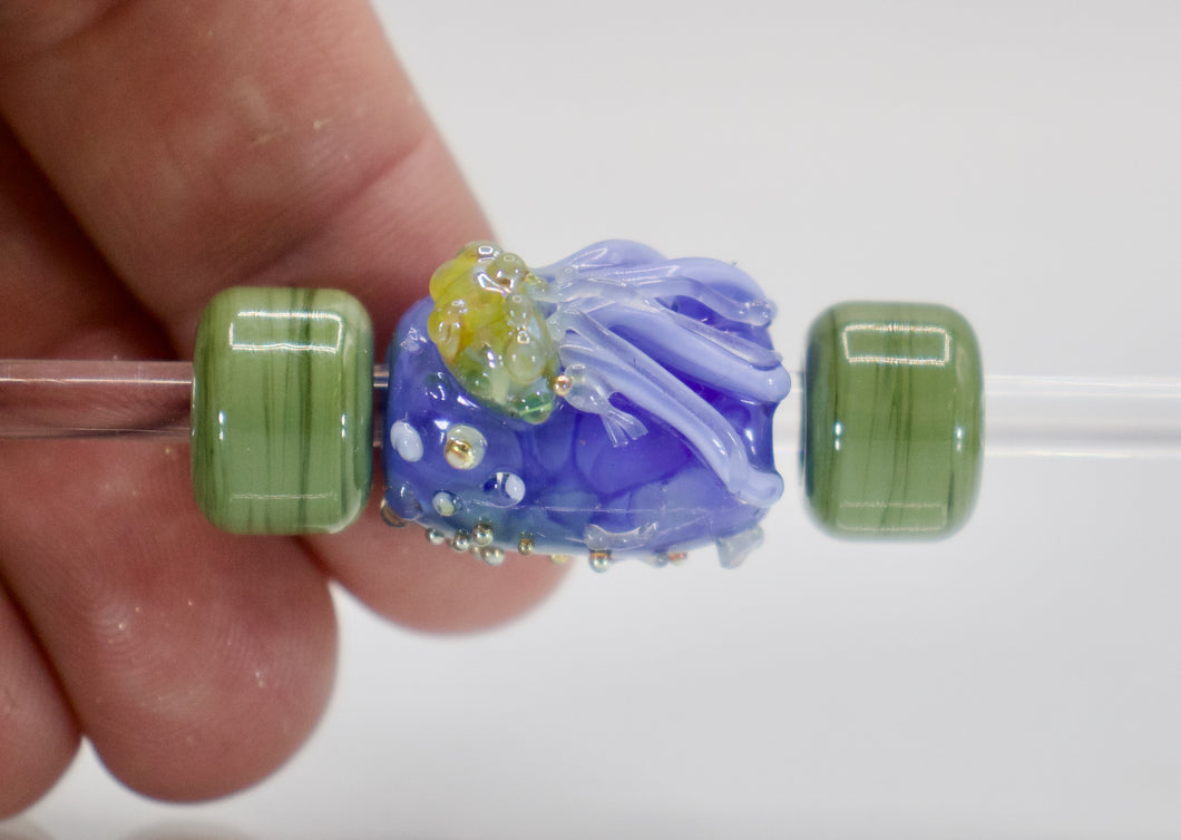 a hand holding a green and blue glass bead