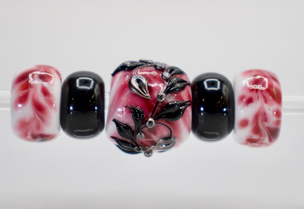 a red and black glass bead with leaves on it